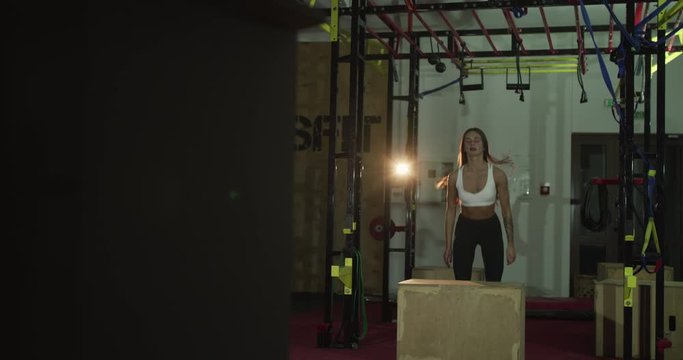 Pretty sports woman training exercise box jumps on wooden crate in a gym