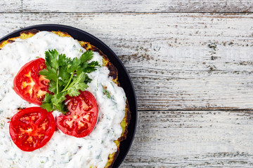 Zucchini cake with tomatoes and fresh parsley on white wooden background.