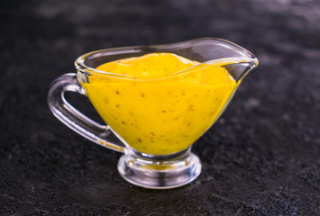 Mustard orange sauce in a glass sauceboat on a black background.Close-up.
