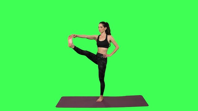 Yoga Instructor practices a series of standing positions on one leg, losses balance and laughs at the end, over green screen. Long shot.