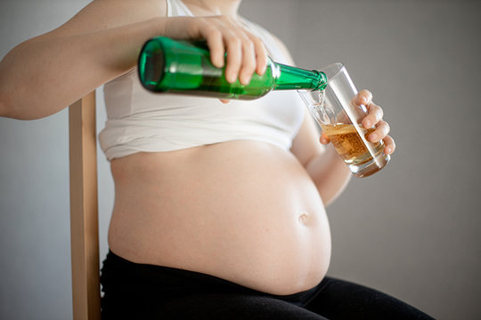 pregnant woman pours a beer ,glass is still empty