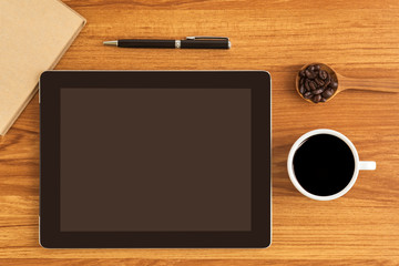 The tablet is placed on a wooden office desk, coffee cup, pen, Top view.