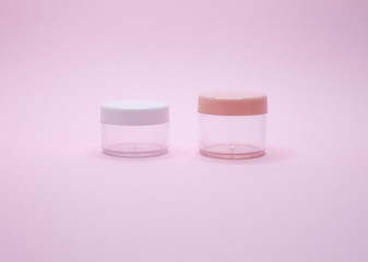 Two empty cosmetic jars on pink background