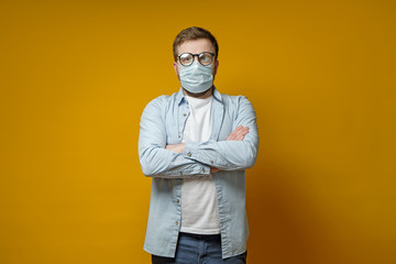 Serious man in a medical mask and glasses, standing with arms crossed and looking confidently....