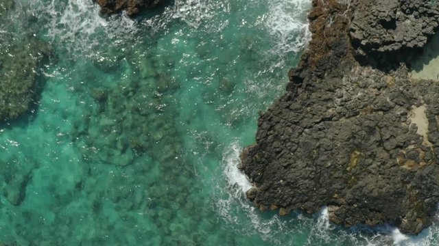 Flying over a rocky coast with waves crashing on the beach in Hawaii.