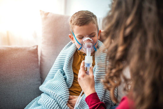 Causian little boy making inhalation with nebulizer at home. Child asthma inhaler inhalation nebulizer steam sick cough and medical concept. Boy having respiratory illness helped by mother
