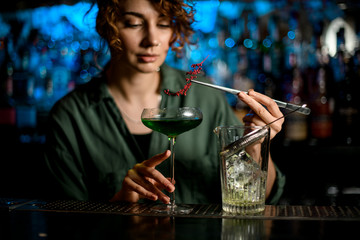 young woman at bar holds glass with cocktail and accurate decorates it