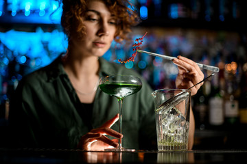 young woman at bar holds glass with cocktail and carefully decorates it