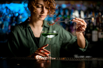 young woman bartender holds glass with cocktail and decorates it