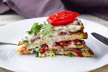 Pice of zucchini cake with tomatoes and fresh parsley on white wooden background.