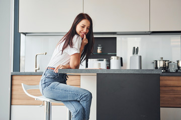 Young beautiful brunette in casual clothes sits in kitchen with fresh drink at morning time