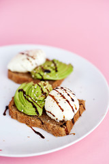 Breakfast toast with poached egg and avocado on the white plate. Pink background
