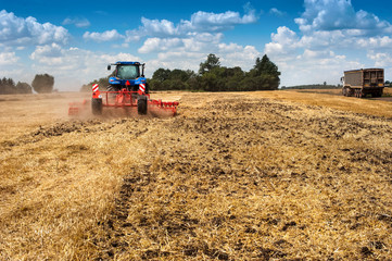 blue new tractor pulls a red harrow in the field, soil preparation