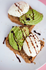 Breakfast toast with poached egg and avocado on the white plate. Pink background