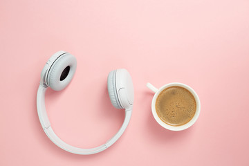 Music or podcast background with headphones and cup of coffee on pink background, flat lay. Top view, flat lay