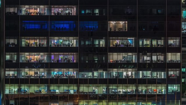 Modern office building with big windows at night timelapse close up view, in windows glowing light shines and some people inside, Singapore. Tilt up
