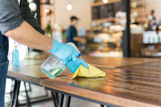 Waiter cleaning the table with disinfectant spray and microfiber cloth in cafe.