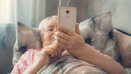 Coronavirus self-isolation advice for over-70s Elders, social isolation and loneliness in older people. Age-group risk for coronavirus. Lonely elderly woman lies in bed at home. - obrazy, fototapety, plakaty