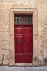 Fototapeta na wymiar Vintage red wooden door in yellow stone wall. Malta