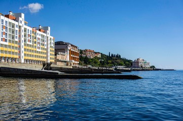 Yalta, Russia - September 30, 2019: View of coastline with breakwaters and hotels along shore against background of Crimean mountains. Selective focus. Clear sea is dark blue.