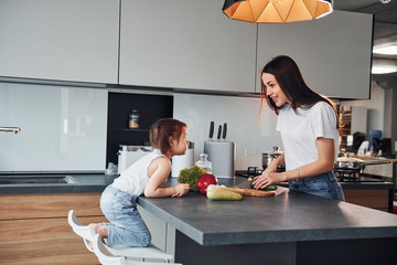 Mother with her little daughter slicing vegetables indoors in kitchen