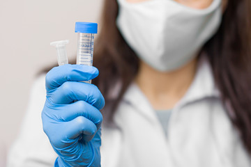 Test tubes with probe on coronavirus, flu, 2019-nCoV, SARS-nCov, COVID-2019 in womans hands. Doctor, wearing blue gloves and protective mask on the face.