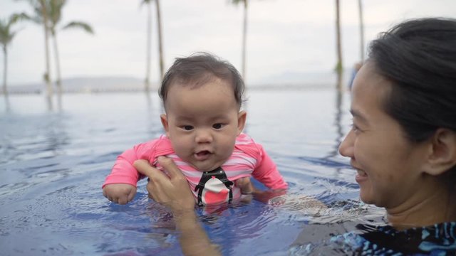 mother holds her baby while learning to swim in the pool