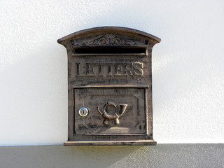 A retro looking gray mailbox, or letterbox, affixed to the exterior white     wall     