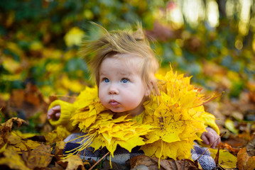 happy little girl laughs and plays outdoors. On the neck there is a necklace of autumn leaves.