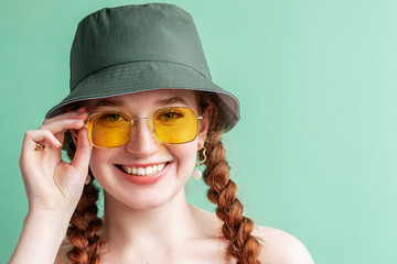 Happy smiling fashionable woman wearing yellow square sunglasses, trendy green bucket hat. Close up portrait. Copy, empty space for text