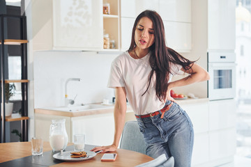 Young beautiful brunette in casual clothes indoors in kitchen at daytime near table with milk and cookies