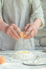 Men's hands break an egg over flour