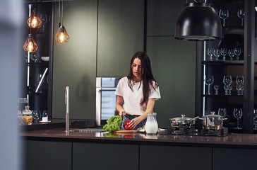 Vegetables and milk on table. Preparing food. Young beautiful brunette in casual clothes indoors in...