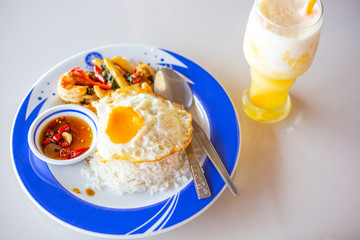 a dish of boiled rice, fried egg and shrimp with sauce on a plate, next to a pineapple smoothie,