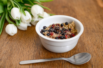Delicious spring breakfast. Oatmeal in bowl on wooden table with tulips.