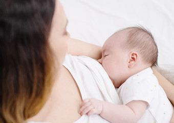 Woman feeding baby. Mother and child on a white bed.