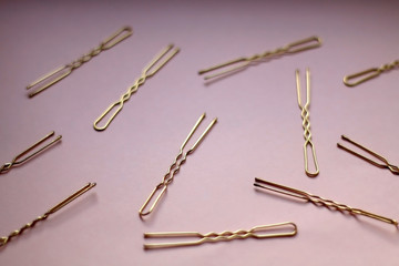 Golden hair clips on pastel pink background. Selective focus.