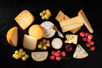Cheese, many different types, shot from above on a black background with grapes