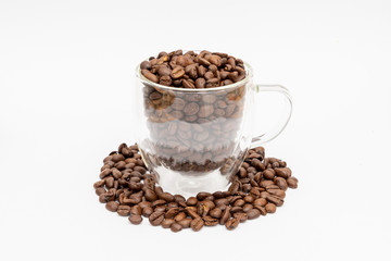 Glass thermos insulating cup transparent overfilled with roasted coffee beans on white underground