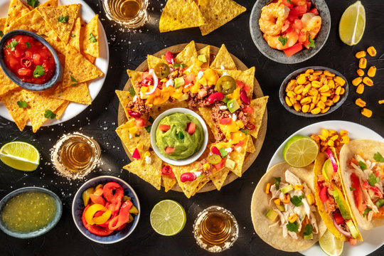 Mexican food variety, shot from the top on a black background. Nachos, guacamole, tequila, tacos etc, a flat lay