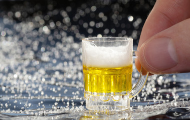 Male fingers holding a miniature beer mug against a bokeh background. Moderate consumption concept