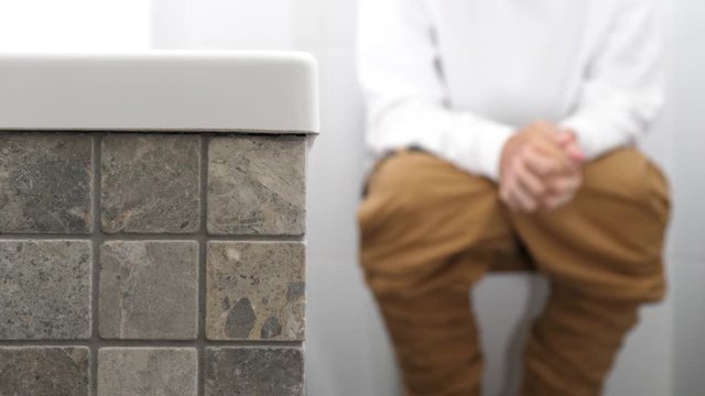 A man with trousers down sitting on the toilet has problems with defecation or kidney stones, he is uptight, clenches his fists.