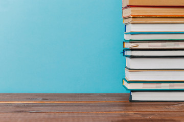 A simple composition of many hardback books, raw books on a wooden table and a bright blue background. Going back to school. Copy space. Education.