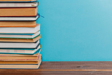 A simple composition of many hardback books, raw books on a wooden table and a bright blue background. Going back to school. Copy space. Education.