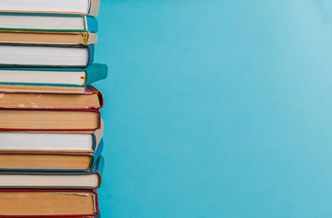 A simple composition of many hardback books, raw books on a wooden table and a bright blue background. Going back to school. Copy space. Education.