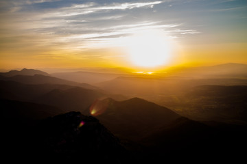 Dark silhouettes of the Carpathian rocky mountains and sunset sky with a large yellow sun