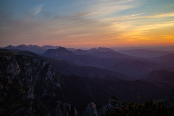 Obraz premium Purple silhouettes of Carpathian rocky mountains and sunset orange-blue sky with clouds