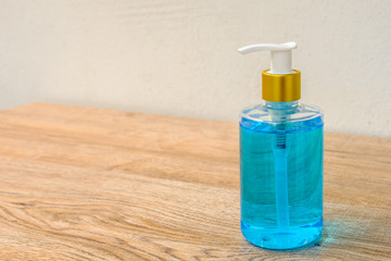 Alcohol gel in a pump bottle placed on a wooden floor beside a white wall.