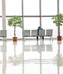 One man sits on a bench near a glass display case in a shopping center.