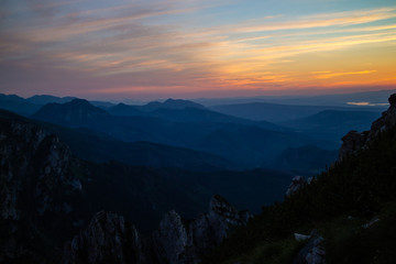 Blue silhouettes of Carpathian rocky mountains and sunset orange-blue sky with clouds